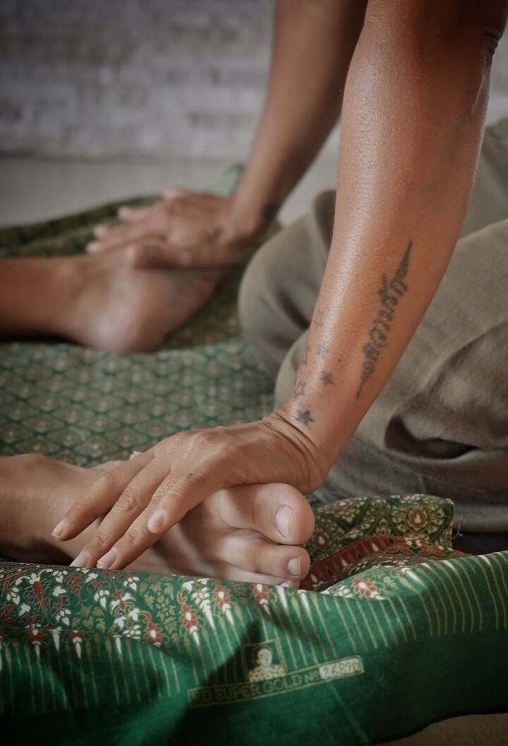 Detalhe da massagem tailandesa tradicional: mãos trabalhando os pés sobre tecido tailandês